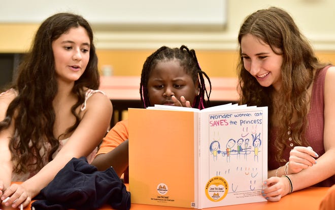 Volunteers (left) Mia Tiller and (right) Nikki Walton sit with Taliah Williams as she gets her first look at her book "Wonder Woman Cat Saves the Princess" at Wednesday's book signing party at the YMCA Tiger Academy on Jacksonville's northwest side, September 20, 2023. High School student Banks Vadeboncoeur and her group of volunteers run the Young Writers Workshop, a youth-led summer program dedicated to fostering a love of creative writing and reading among underserved children in Jacksonville. At the end of the workshop, each child wrote and published their own hardcover book.