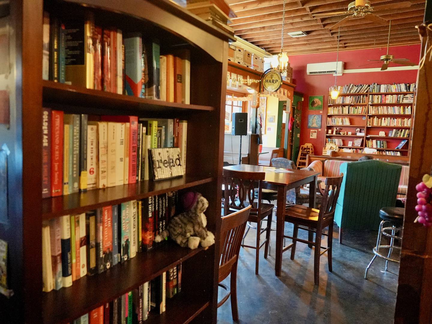 a bookshelf in the foreground with tables and armchairs of a cozy pub in the background