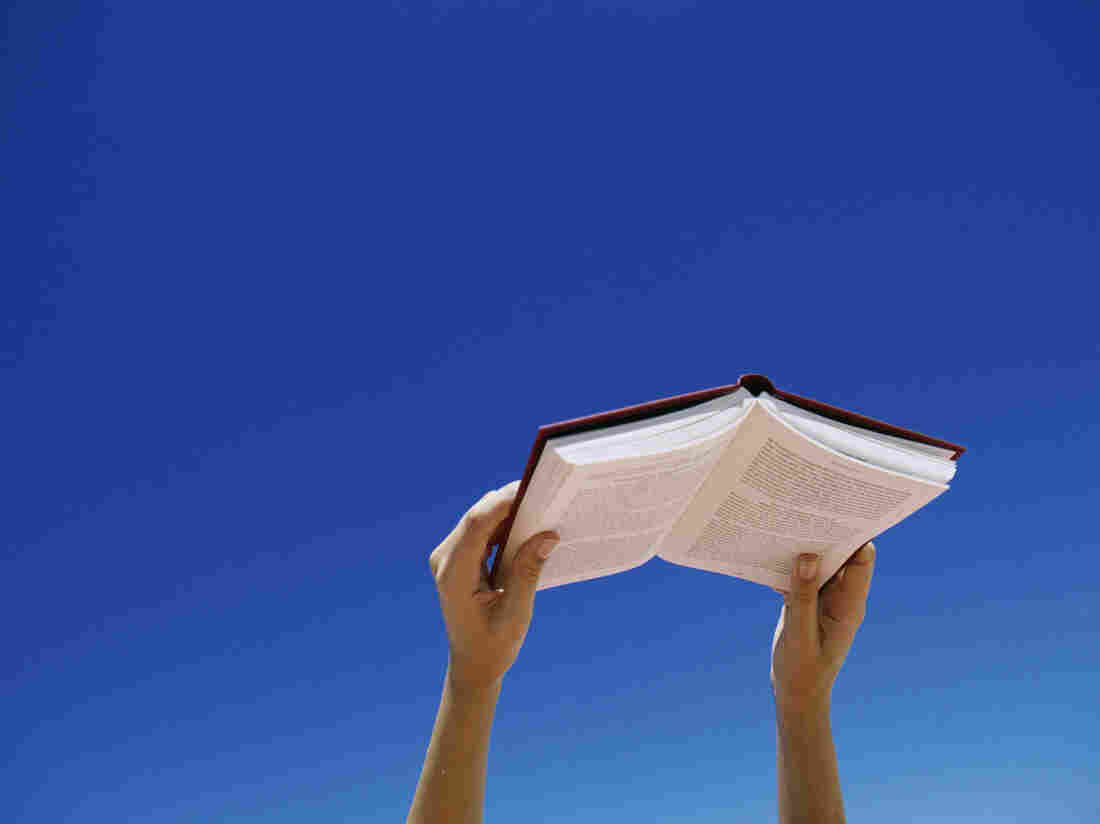 Two hands hold open a book against a bright blue sky.