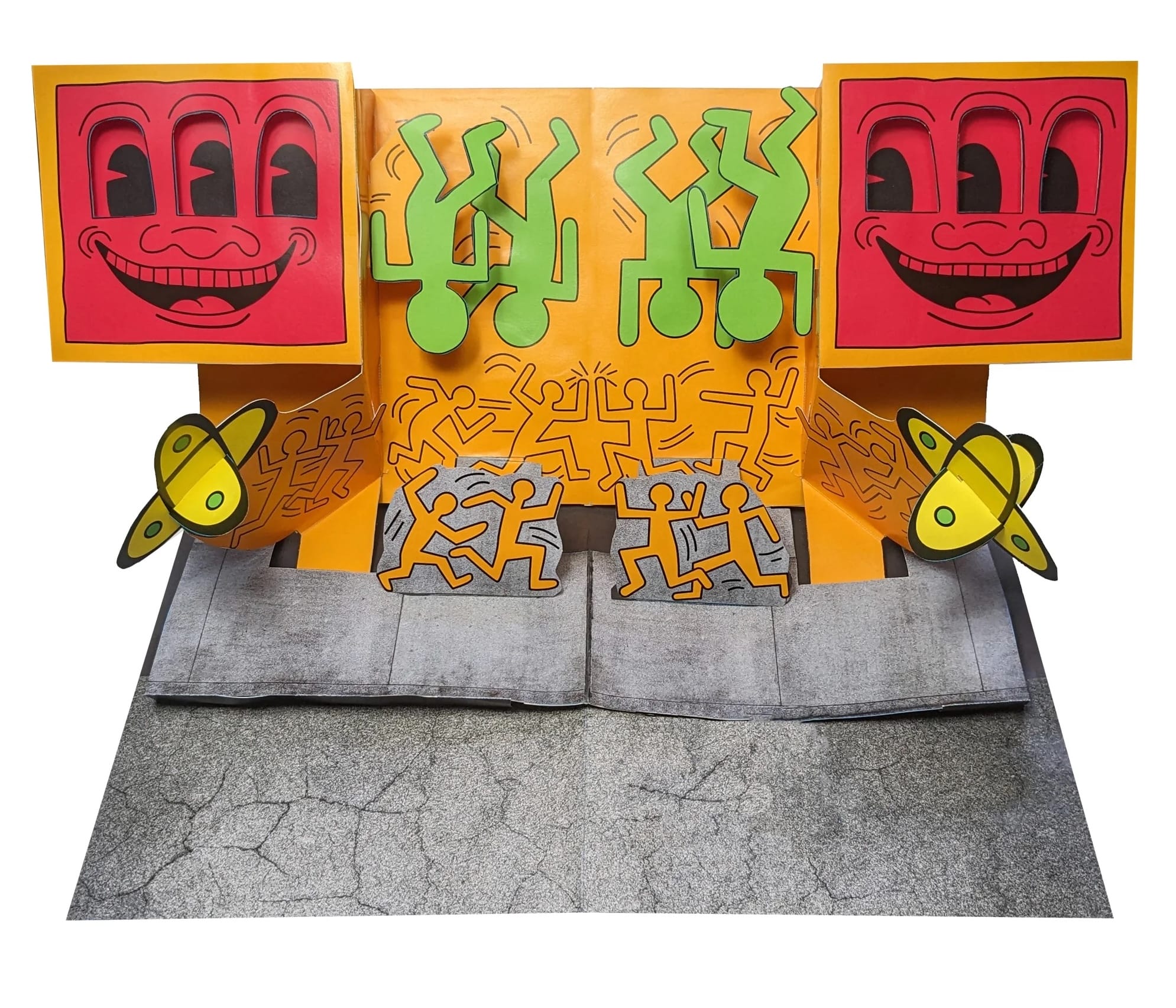 a pop-up paper spread from a pop-up book of artwork by Keith Haring, this piece depicting a recreation of a street mural with smiley faces that have three eyes, upside-down green dancing figures, planets, and tiny running figures in orange
